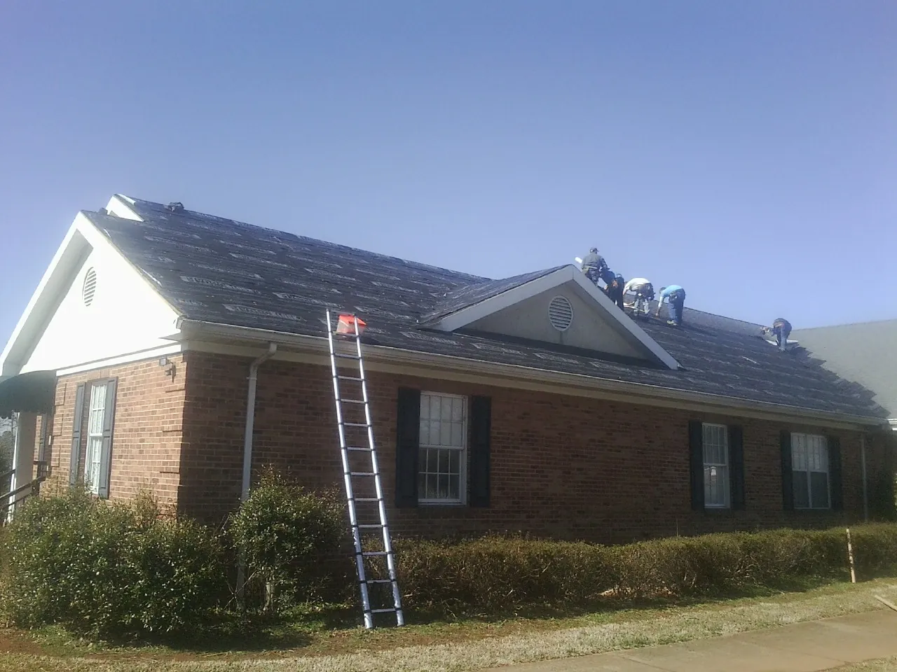 Crew tearing shingles off a brick ranch roof with a ladder set — Metal Roof Repair work by our crew in Nauvoo