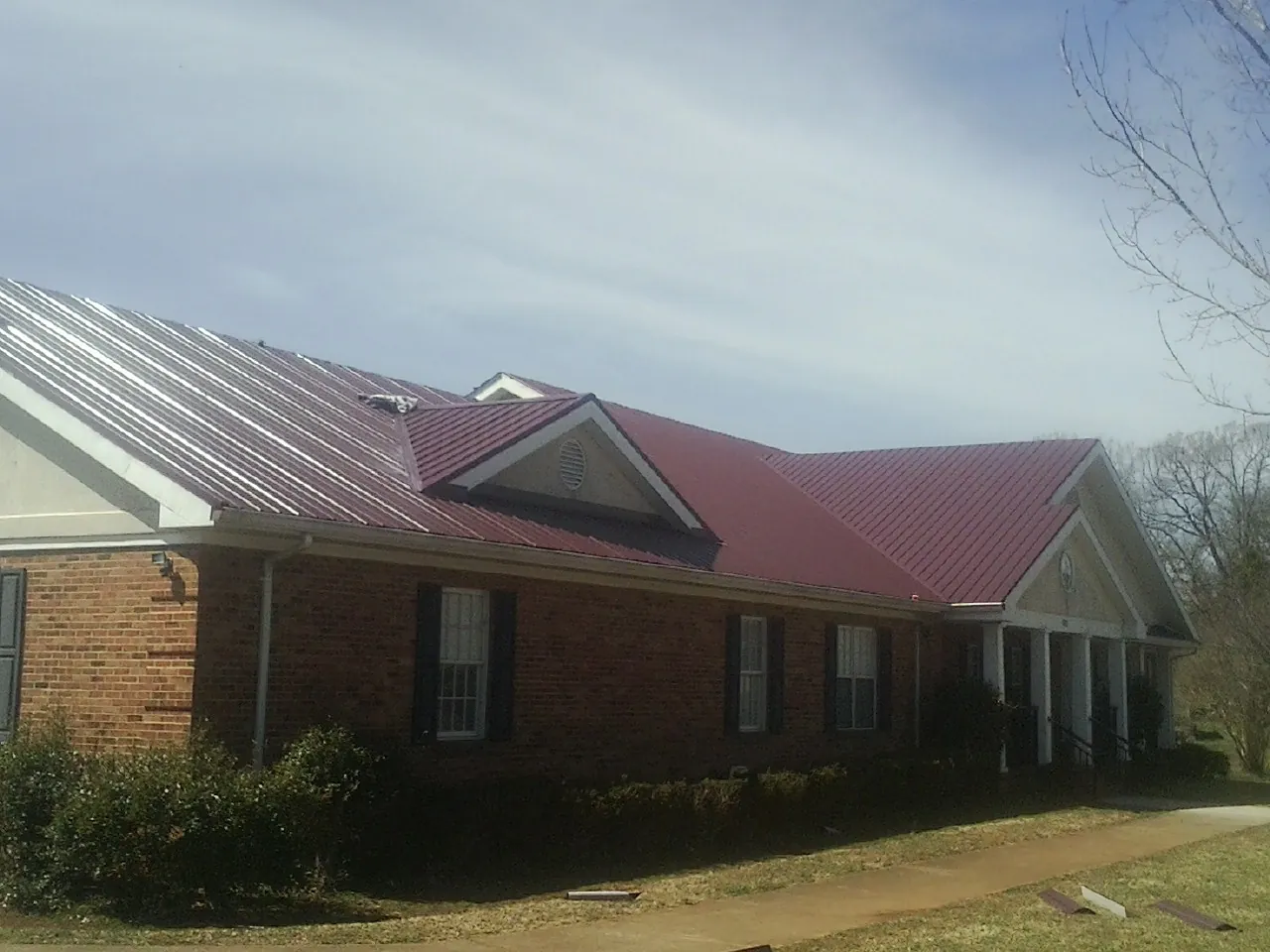 Red metal roof with gabled entries on a long brick building, from a Hail Damage Roof Repair job in Nauvoo