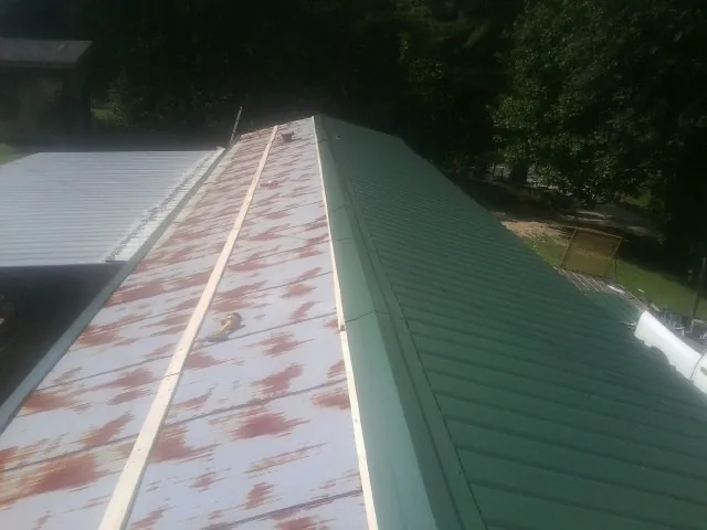 Old rusted panels beside newly installed green metal roofing — Wind Damage Roof Repair by Roofing Brothers in Nauvoo