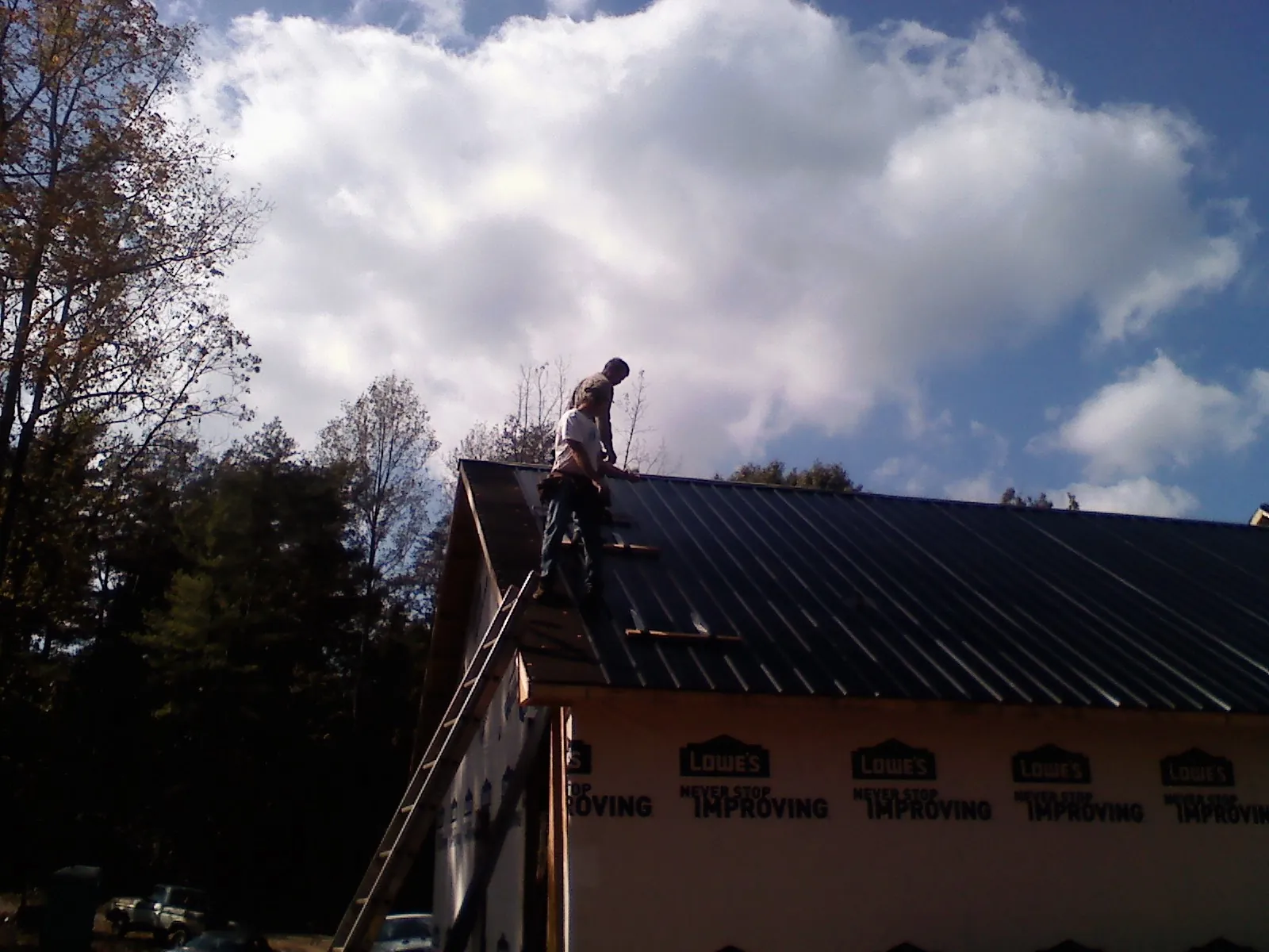 Roofer fastening dark metal panels high against a cloudy sky, from a Roof Inspection job in Nauvoo