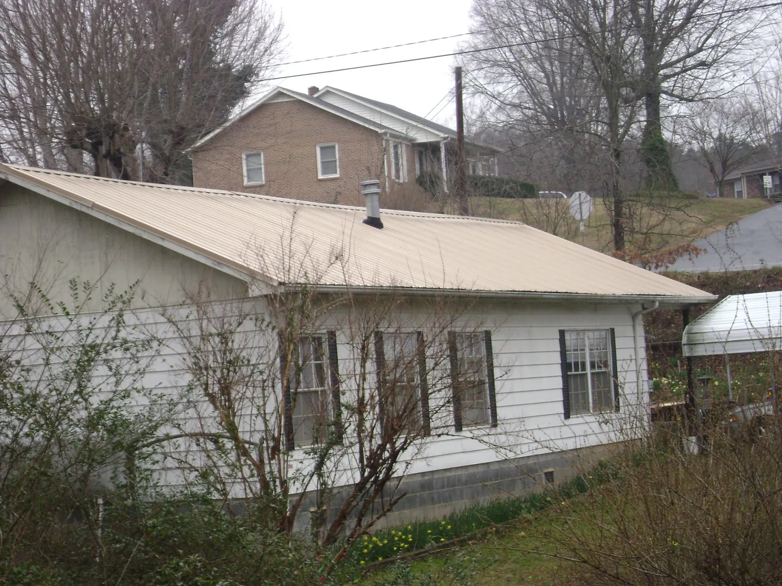 Tan metal roof on a white sided house set into a hillside — Commercial Roofing by Roofing Brothers in Nauvoo
